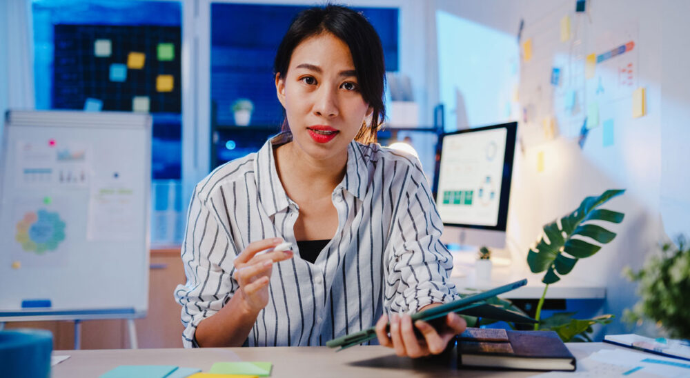 asia businesswoman social distancing new normal virus prevention looking camera presentation colleague about plan video call while work office night